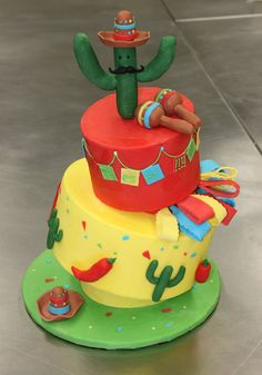 a three tiered cake with decorations on it's sides and cactus topper