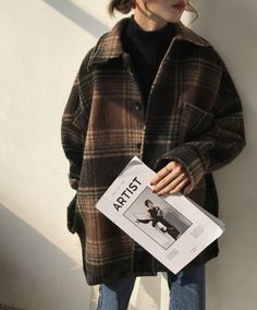 a woman standing against a wall holding a magazine