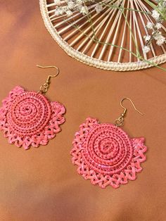 pink crochet earrings on a brown surface next to a wicker basket with flowers