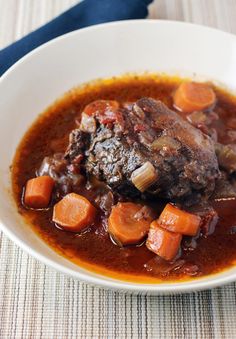 a white bowl filled with stew and carrots on top of a tablecloth next to a fork