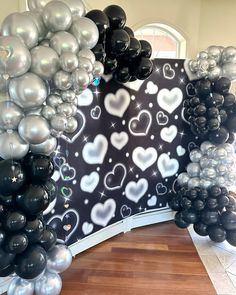 black and silver balloons are on display in front of a wall with white heart shapes