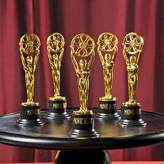 five golden trophies sitting on top of a black tray in front of a red curtain