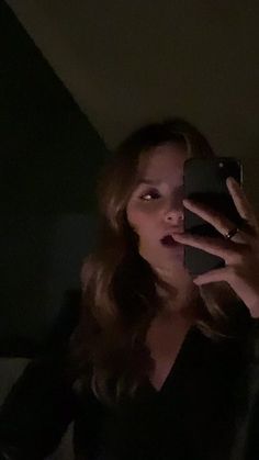 a woman is taking a selfie in the dark with her cell phone while wearing a black shirt