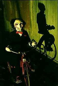 a creepy clown riding a bike in front of a shadow of a man on the wall