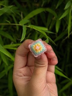 a hand holding a small crocheted flower in front of some green plants and grass