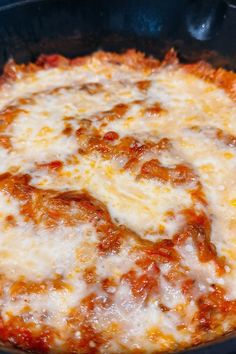 a pizza with cheese and tomato sauce in a black pan on a stove top oven