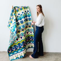 a woman standing next to a colorful blanket on top of a wooden pole in front of a white wall