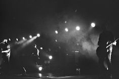 black and white photograph of people playing instruments on stage at night with lights in the background