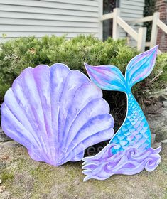 a blue and purple mermaid tail sculpture sitting on top of a rock next to a house