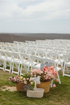 an outdoor ceremony set up with white chairs and flower baskets on the grass in front of them