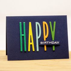 a birthday card with the words happy written on it in multicolored letters, sitting on a wooden surface