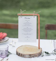 a menu is displayed on a wood slice at a table with glasses and napkins