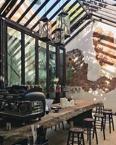 an indoor dining area with wooden tables and stools in front of large windows that have exposed brick walls