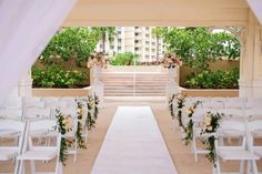 an outdoor wedding setup with white chairs and floral arrangements on the aisle leading up to the ceremony venue