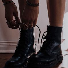 black and white photograph of person wearing boots with chains on their ankles, standing in front of wall