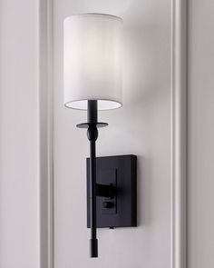 a wall mounted light with a white shade on it's face and black arm