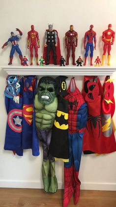 there are many superheros on the shelf and one is in front of them with capes