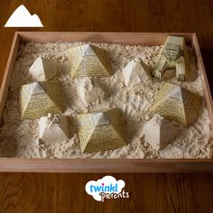 an open box filled with sand and paper cut into pyramids on top of it