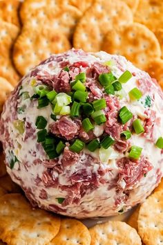 a cheese ball covered in meat and green onions on top of crackers