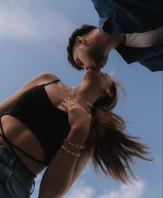 a man and woman kissing each other in front of a blue sky with white clouds