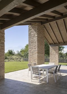 an outdoor dining table and chairs under a pergolated patio with stone pillars on either side