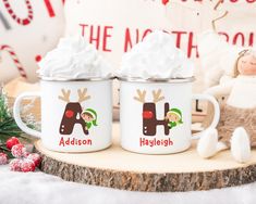 two personalized christmas coffee mugs with reindeer faces on them, sitting next to a teddy bear