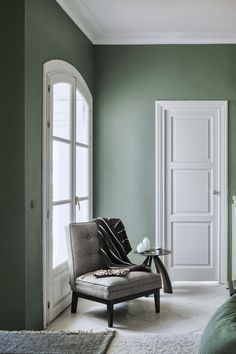 a bedroom with green walls and a chair in front of the door that leads to another room