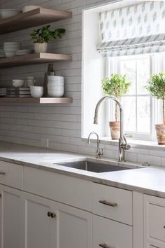 a kitchen with white cabinets and open shelving above the sink is decorated with potted plants