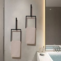 three towels hanging on the wall next to a bathtub in a room with white walls