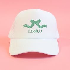 a white hat with green ribbon and the word aphi on it against a pink background