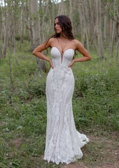 a woman standing in the woods wearing a wedding dress with an open back and straps