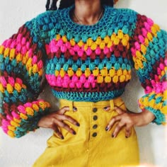 a woman with her hands on her hips wearing a colorful knitted sweater and yellow skirt