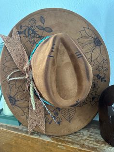 These custom hand burned wide brim western hats features a fabric hand tied band, turquoise beading, and feathers. Every hat is customizable free of charge so please reach out to me via message so we can get a beautiful hat made for you. THE HAT PICTURED IS SOLD BUT I CAN MAKE ONE FOR YOU JUST LIKE IT. All designs are on the top of the hat unless otherwise asked. The band color is also customizable, so if you would like a specific color please let me know.  THE HAT LISTED IS CAMEL This hat is NOT a Charlie1Horse hat, and the price reflects that. The hat is 65% cotton 35% polyester. It is a vegan faux suede.  All hats are one size fits most with an adjuster tie on the inside. The hat is 22.8" or 57cm at its largest.  ALL HATS ARE MADE TO ORDER. NO HAT WILL BE 100% THE SAME DUE TO HAND BURNI Turquoise Bohemian Hat For Western-themed Events, Turquoise Country Hat For Western-themed Events, Turquoise Bohemian Fedora, Artisan Turquoise Hats For Western-themed Events, Artisan Turquoise Hat For Western-themed Events, Turquoise Bohemian Hat For Kentucky Derby, Hat Burning, Hand Burn, Western Hat