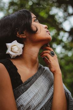 a woman with black hair and a white flower in her ear is looking up at the sky