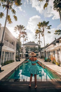 a woman standing in front of a pool surrounded by palm trees