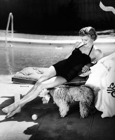 a black and white photo of a woman sitting on a chair next to a pool