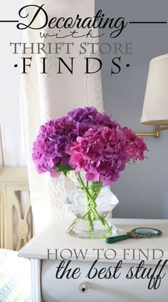 a vase filled with purple flowers sitting on top of a white table next to a lamp