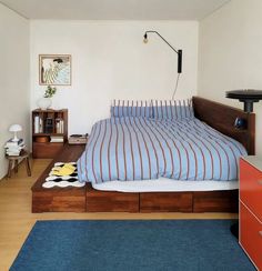 a bed sitting in a bedroom next to a blue rug and wooden dresser under a lamp