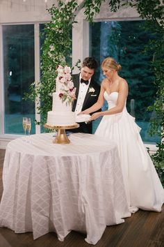 a bride and groom are cutting their wedding cake at the reception table with greenery around them