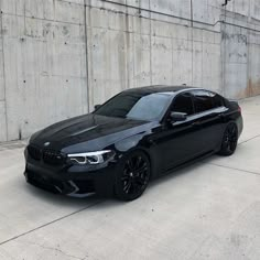 a black bmw is parked in front of a concrete wall with no people around it