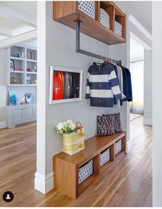 a wooden bench sitting in front of a wall with clothes hanging on it's hooks