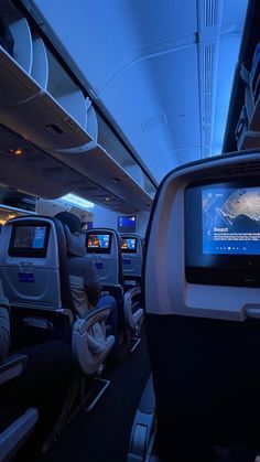 the inside of an airplane with many seats and televisions on each side of the aisle