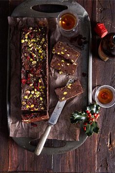 a tray topped with brownies next to two cups of tea and a knife on top of a wooden table