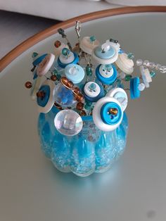 a vase filled with lots of blue and white buttons on top of a glass table