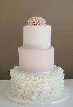 a three tiered white and pink wedding cake with flowers on the top, sitting on a table