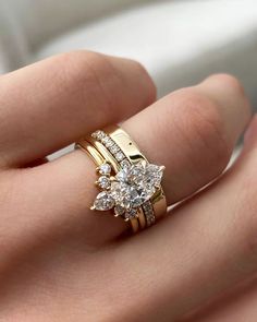 a woman's hand holding a gold ring with three stones on it and two diamonds in the middle