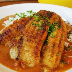 two pieces of fish in a red sauce with rice and parsley on the side