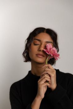 a woman holding a pink flower up to her face