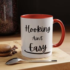 a red and white coffee mug sitting on top of a wooden table next to a spoon