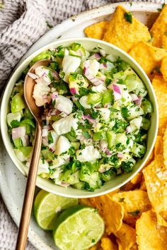 a white bowl filled with guacamole and tortilla chips next to a wooden spoon